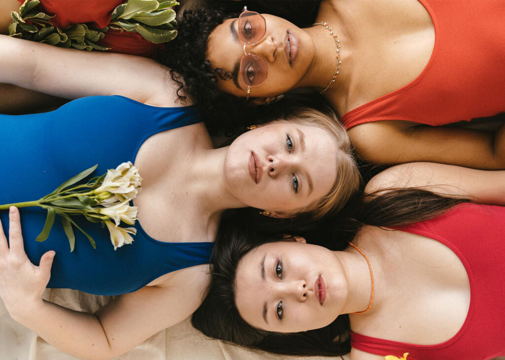 Le body-positivity pour les petites poitrines : ce que ça change au quotidien 7 Trois femmes aux morphologies et styles différents allongées ensemble, illustrant la beauté de la diversité et l'unité.