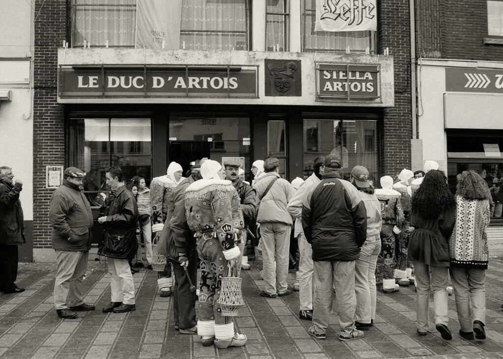 Une foule réunie devant un établissement nommé "Le Duc d’Artois", illustrant un moment de vie sociale et de communauté.